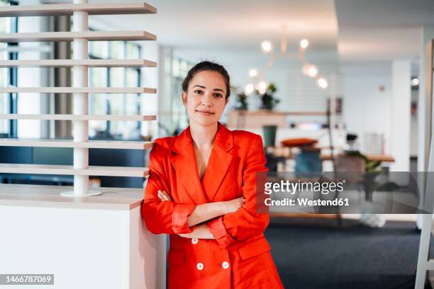 smiling businesswoman with arms crossed standing in office - roter anzug stock-fotos und bilder