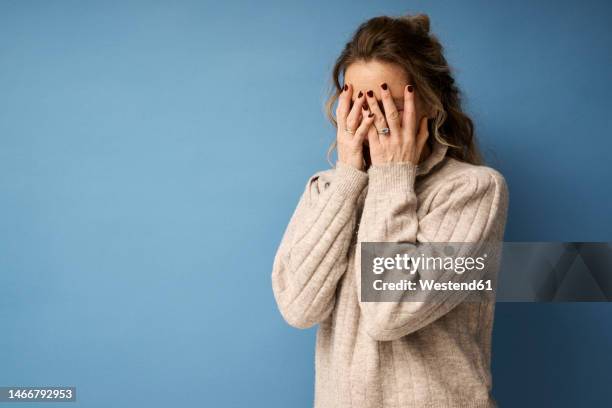 woman covering face with hands against blue background - awkward bildbanksfoton och bilder
