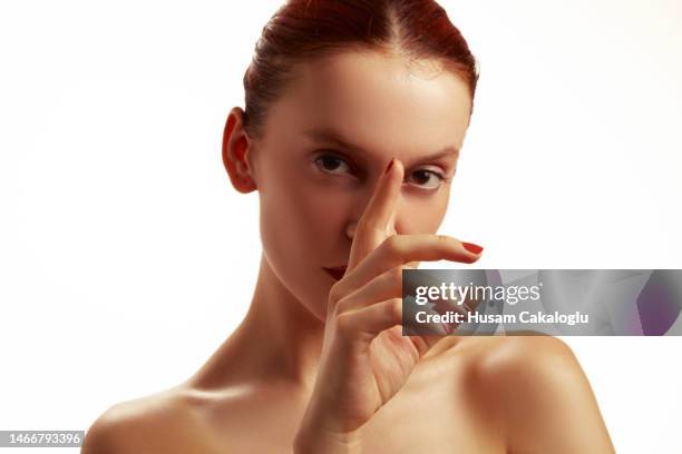 young woman with red hair looking at camera through fingers, hand on face. - illuminati 個照片及圖片檔