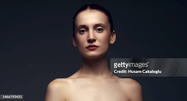 Portrait of expressionless young woman with serious posture in front of black background.