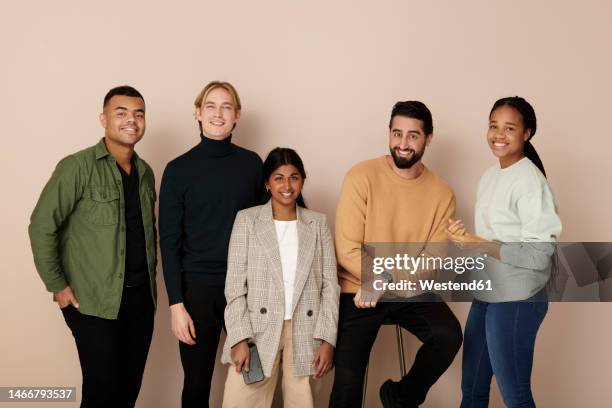 smiling multiracial business colleagues posing against beige background - organised group photo stock pictures, royalty-free photos & images