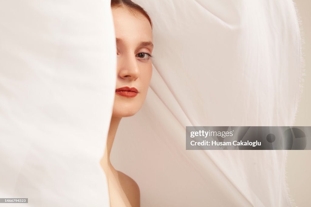Retrato de una mujer joven mirando emocionalmente a la cámara a través de una tela blanca que fluye.