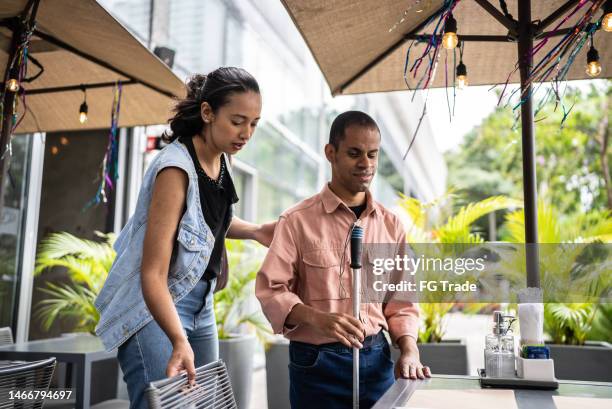 mid adult woman helping a visually impaired man sitting in the chair - assiste stock pictures, royalty-free photos & images