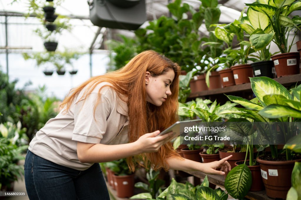 Young woman analyzing plants while use digital tablet in a garden shop