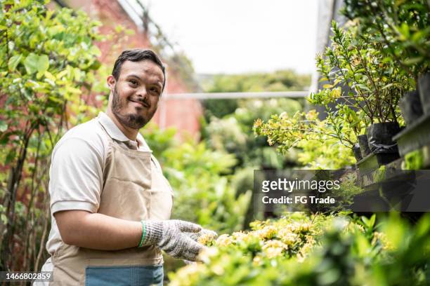 portrait of young special needs botanist taking care of plants in a garden center - disabilitycollection stockfoto's en -beelden