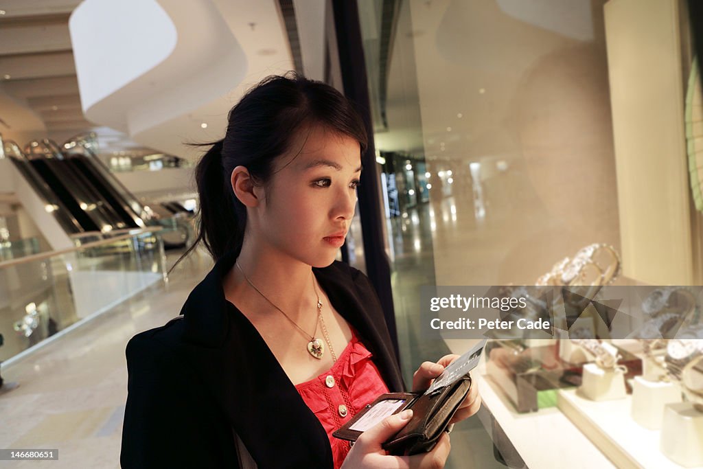 Woman looking in shop window holding credit card