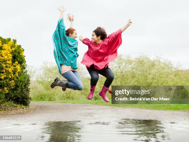 women jumping mid air in large puddle - raincoat stockfoto's en -beelden