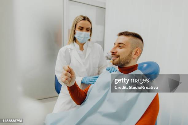 glücklicher männlicher patient, der nach der zahnbehandlung in den spiegel schaut - dentalimplantat stock-fotos und bilder