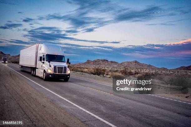 semi-remorque blanche circulant sur une autoroute à deux voies au crépuscule sous un magnifique paysage nuageux dans une région désertique vallonnée du sud-ouest des états-unis avec les phares allumés - interstate 70 photos et images de collection