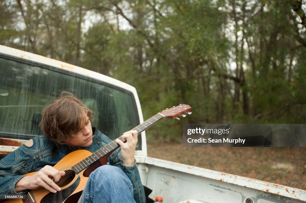 Teenager Sitting in Truck Bed Playing Guitar