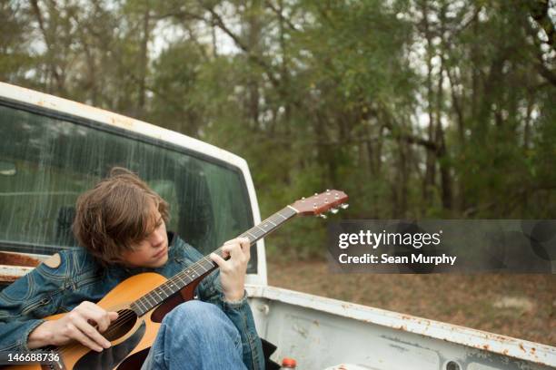 Teenager Sitting In Truck Bed Playing Guitar, Foto de stock