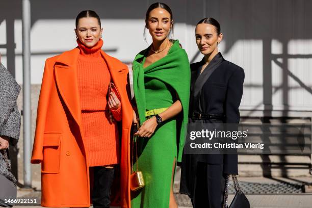 Valerie Lipovetsky wears orange knit turtleneck, coat, skirt & Tamara Kalinic wears green coat, belt, cape, golden mini bag & Olivia Perez wears...