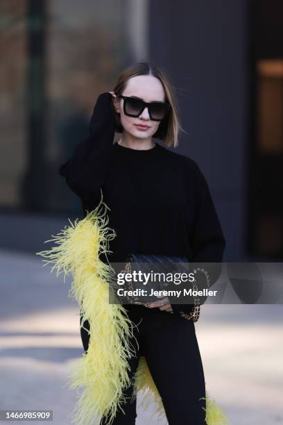Katya Bychkova seen wearing Louis Vuitton black sunglasses, The Attico black knit sweater with yellow feather boa detail, Coperni black short pants...
