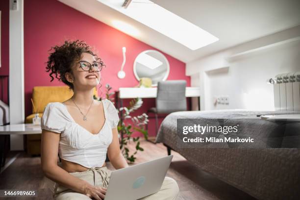 eine junge studentin studiert in ihrer wohnung, schaut auf den laptop und die bücher und papiere neben ihr - student girl using laptop computer and smart phone stock-fotos und bilder