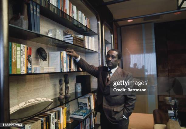 John H Johnson , publisher of Ebony magazine and owner of the Johnson Publishing Company, standing next to book shelves in his office in Chicago in...