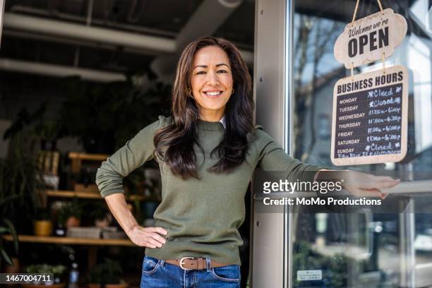 portrait of proud female flower shop owner in front of open sign - small business stockfoto's en -beelden