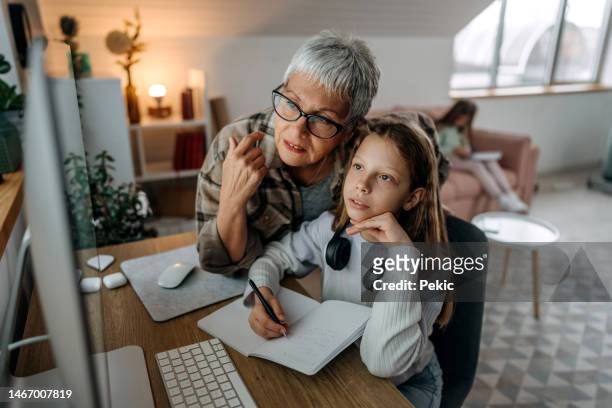 grandmother helping granddaughter with homework while she's studying at home - grandma invoice stock pictures, royalty-free photos & images