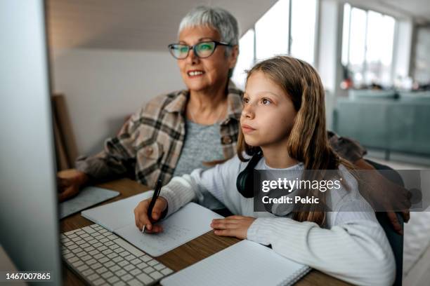 grandmother helping granddaughter with homework while she's studying at home - grandma invoice bildbanksfoton och bilder