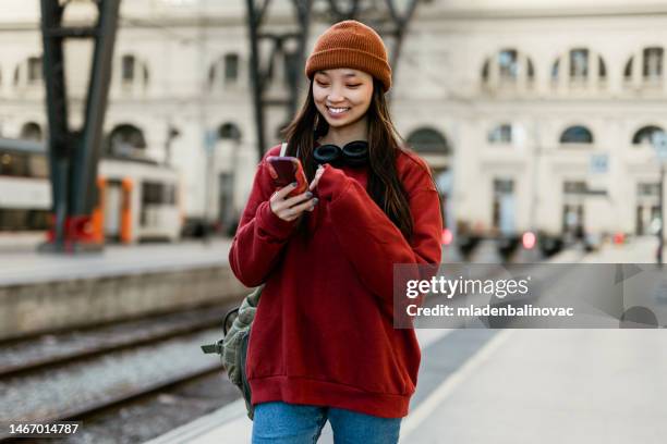 young hipster asian woman using smart phone at the rail station - plataforma de estação de metro imagens e fotografias de stock
