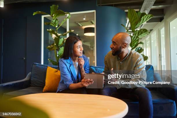 empresarios hablando por una tableta mientras están sentados en el sofá de una oficina - vestimenta casual fotografías e imágenes de stock