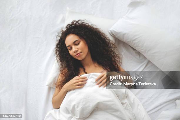 a black woman lies in bed. white linens. dream. cheerful morning. good dream. soft bed. orthopedic mattress. - sleeping woman stock pictures, royalty-free photos & images