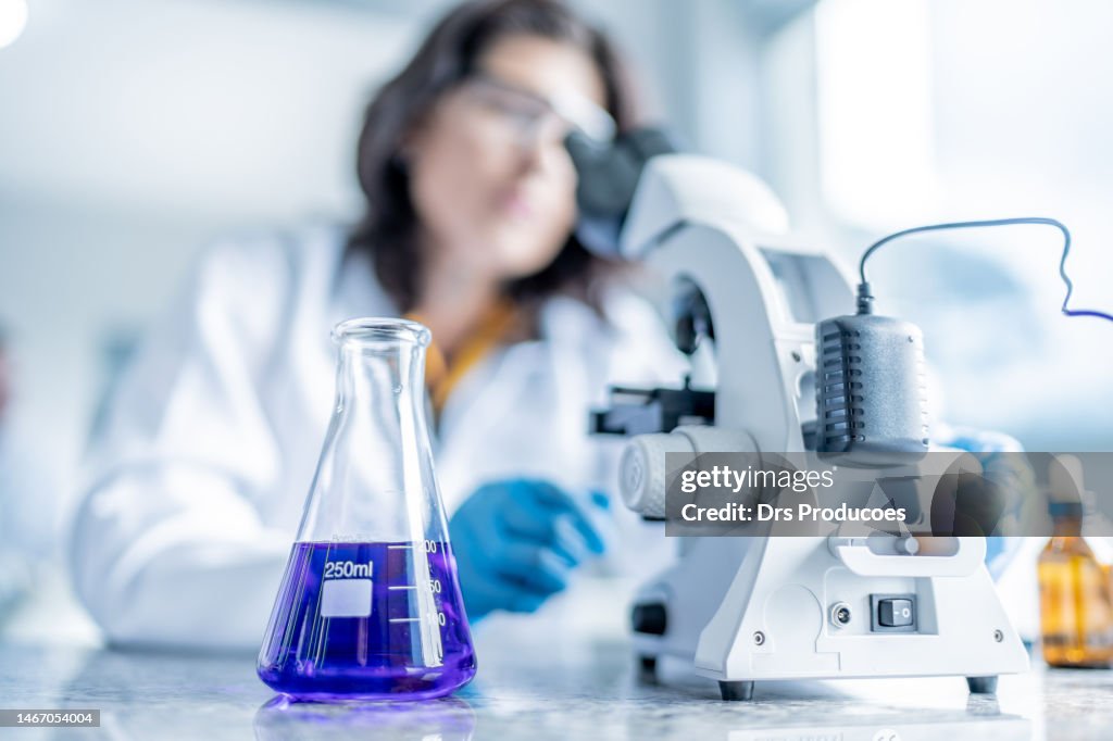 Adult female student analyzing liquid under microscope
