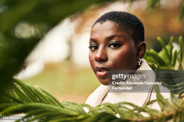 african american woman with short hair and piercings among the leaves of a plant outdoors looking at camera - septum stock pictures, royalty-free photos & images