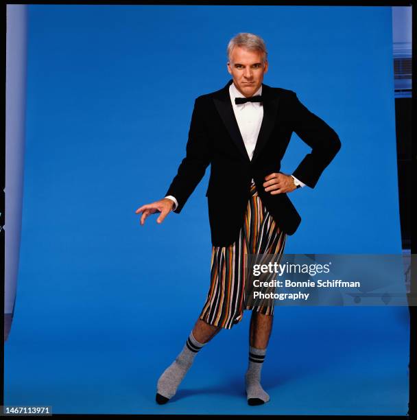 Steve Martin stands in front of blue backdrop in a suit jacket and bowtie with colorful shorts and grey socks in Los Angeles in 1984.