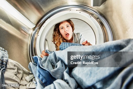 Seen from inside a tumble dryer, beautiful young woman looks horrified as she examines her laundry