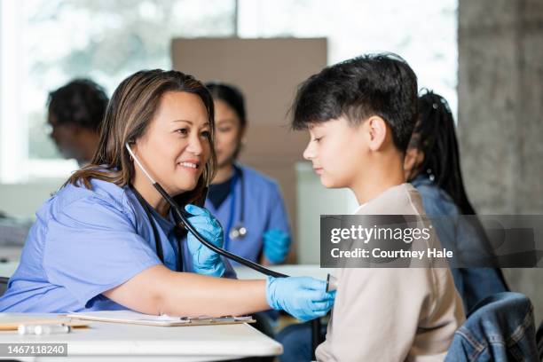 teen boy gets a check-up from a nurse who is volunteering at a community health fair - exhibition stock pictures, royalty-free photos & images