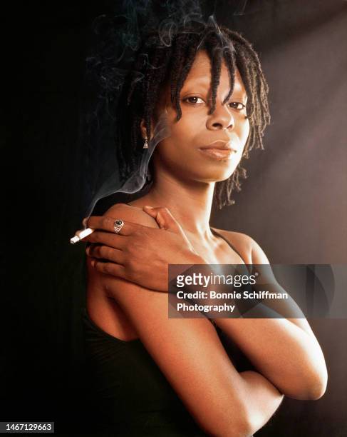 Actor Whoopi Goldberg poses in a black tank with lit cigarette in her hand in Los Angeles in 1985.
