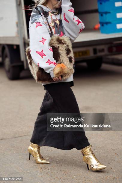 Guest wearing a long black maxi skirt, light grey sweater with a pink, yellow, and dark grey pattern, golden long boots, and fur bag outside Fashion...