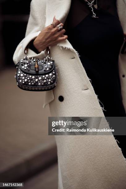 Guest wearing a long black dress, a long white coat, a black balaclava, and mini bag with metal decorations outside Fashion east fashion show during...