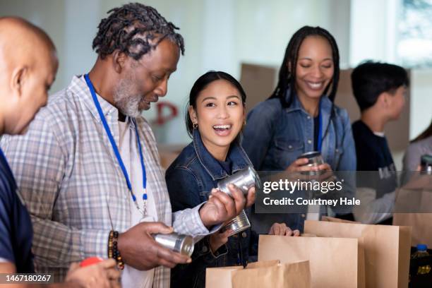 un grupo diverso de voluntarios empaqueta comestibles para la comunidad en el banco de alimentos - food pantry fotografías e imágenes de stock