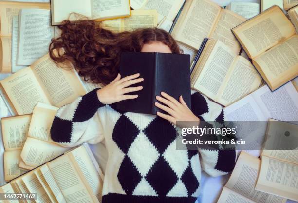 portrait of a teenage girl lying down covering her face with a book surrounded by many books - surrounding ストックフォトと画像