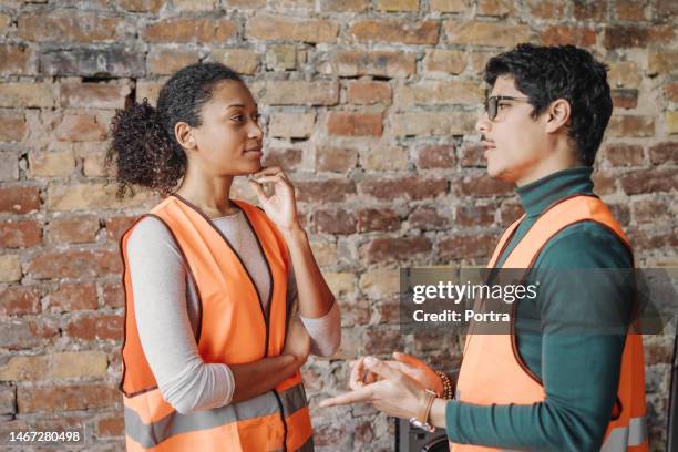 two young engineers in reflective vests talking against brick wall - face to face communication stock pictures, royalty-free photos & images
