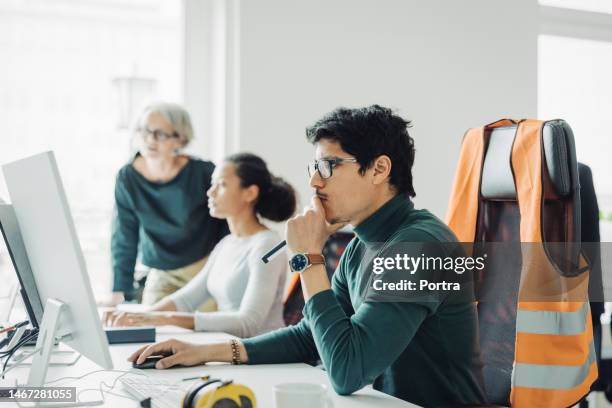 architect working on computer with colleagues in background at engineering office - reflective clothing 個照片及圖片檔