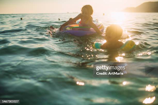 children having fun on summer vacations, swimming, splashing and playing in the sea with inflatable ring - embrace imagens e fotografias de stock