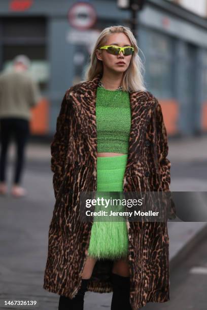 Betty Bachz seen wearing a green cropped top with a matching green mini skirt, high black boots, an animal printed long coat and green shades before...