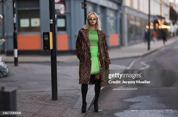 Betty Bachz seen wearing a green cropped top with a matching green mini skirt, high black boots, an animal printed long coat and green shades before...