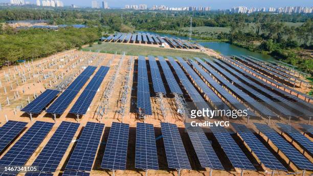 Aerial view of workers installing solar panels atop agricultural fields at the construction site of an agrivoltaic farm in a zero-carbon...