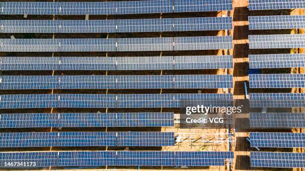 Aerial view of workers installing solar panels atop agricultural fields at the construction site of an agrivoltaic farm in a zero-carbon...