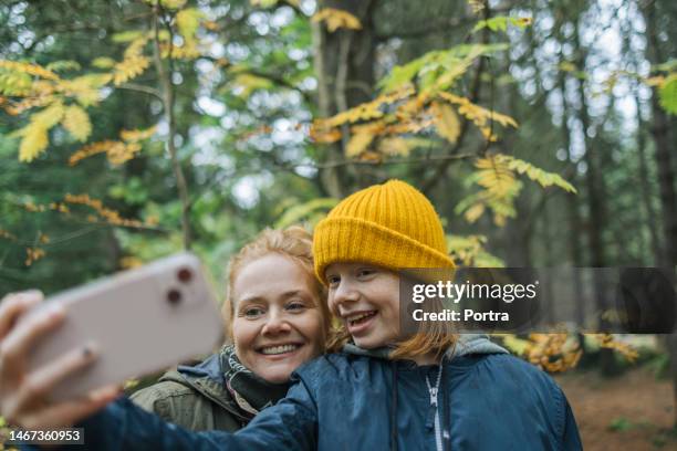 mother and daughter taking selfie in forest on autumn day - selfie girl stockfoto's en -beelden