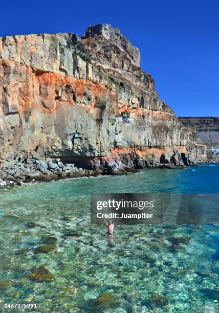 a lonely man, with arms raised,  enjoys a day of sun  in the beach of mogán, gran canaria - ilha de gran canaria imagens e fotografias de stock