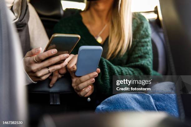 two young women riding in the back seat of a taxi and showing each other memes and data on smart phones - meme text stock pictures, royalty-free photos & images