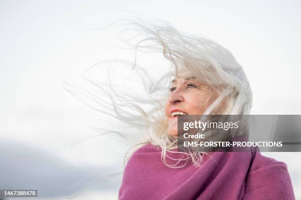 portrait of senior woman standing in sand dunes and enjoying wind - long hair wind stock pictures, royalty-free photos & images