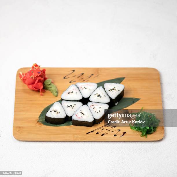 sushi rolls of triangular shape are laid out in form of flower on bamboo leaves. set on wooden board with ginger, wasabi, hiyashi seaweed. japanese food. white background. top view. copy space - folha de bambu - fotografias e filmes do acervo