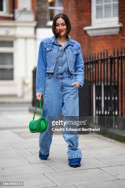 Tiffany Hsu wears a blue denim jumpsuit, a blue denim jacket, a green bag, outside 16Arlington, during London Fashion Week February 2023 on February...
