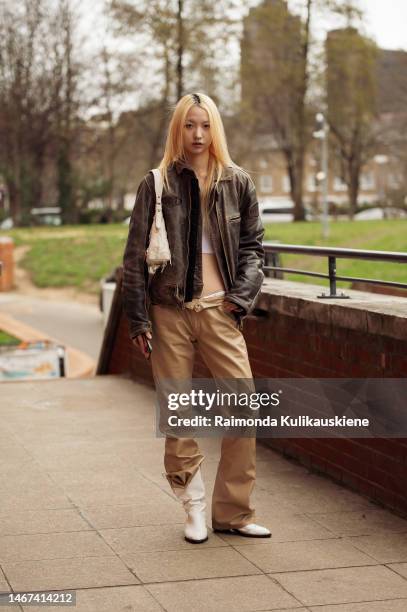 Guest wearing beige leather pants, white cowboy style shoes, white crop top, brown destrest leather jacket and white bag outside Eudon Choi, during...