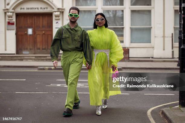 Couple walking together, a man wearing green pants, green shirt, black and green shoes and a girl wearing a lime green dress, silver boots, white...